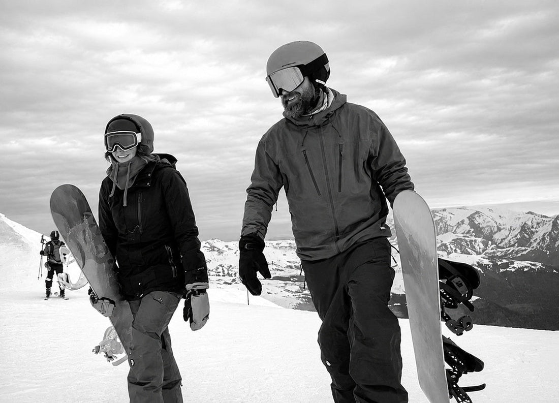 Two snowboarders walking on the mountain carrying their snowboards